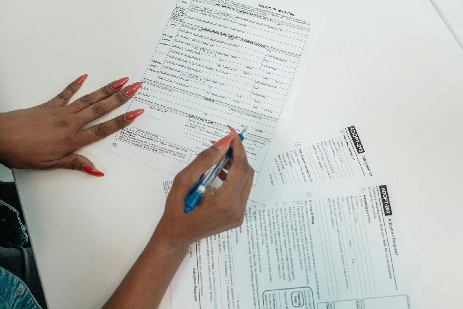 A woman with red nails fills out adoption application forms on a desk.